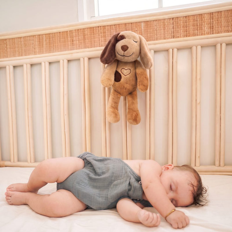 A baby asleep in a cot with a Lulla Pup held by a safe sleep attachment